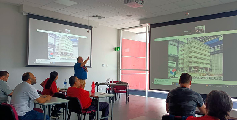 Se muestran varias personas hombres y mujeres, sentados viendo una presentación, hay un expositor, señalando y explicando su presentación